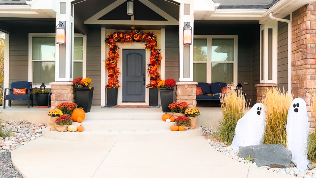 Fall porch with jack-o-lantern garland, mums and decorative ghosts.